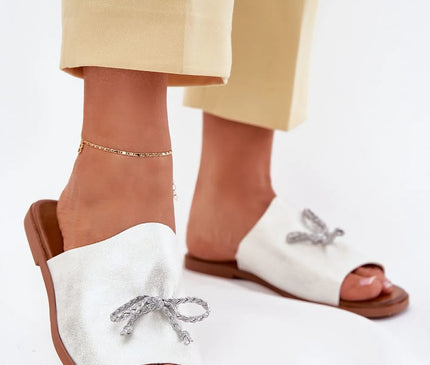 Sandales minimalistes blanches inspirées du Brésil, avec un nœud artisanal gris en détail, design léger parfait pour un style bohème-chic. Modèle idéal pour une balade en bord de mer ou un look urbain tropical, évoquant l'élégance décontractée des plages de Copacabana.
