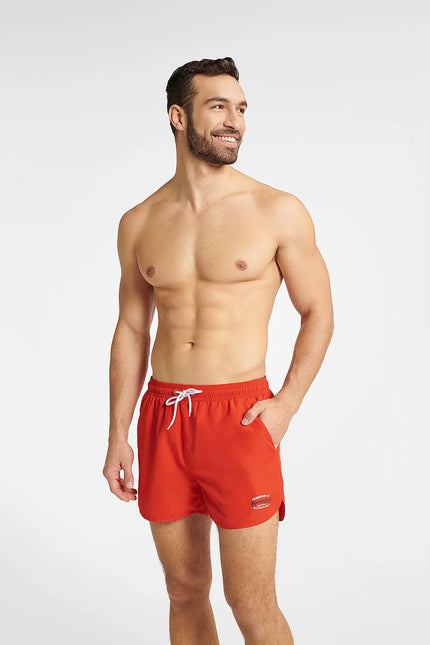 Homme portant un short de bain rouge GUILD à séchage rapide, avec une taille élastique réglable et des détails contrastés. Modèle confortable et tendance, idéal pour la plage et les activités aquatiques. Disponible en tailles M, L, XL, XXL.