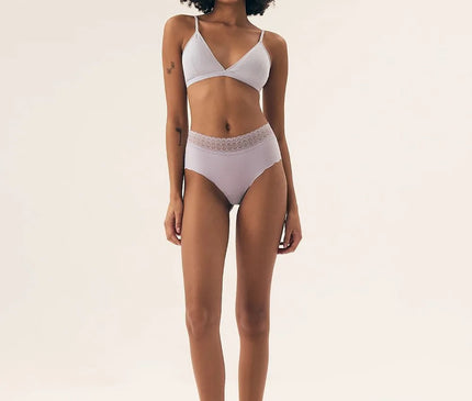 Femme portant un ensemble de lingerie brésilienne élégant et épuré, composé d'un soutien-gorge à bretelles fines et d'une culotte taille haute ornée de détails délicats. Inspiré par l'esthétique naturelle et la sensualité des plages de Rio, cet ensemble met en valeur le confort et la joie de vivre caractéristique du Brésil.
