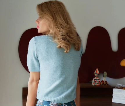 Femme de dos portant un haut bleu pastel à manches courtes et une culotte taille haute avec un imprimé floral tropical inspiré du Brésil, symbolisant la mode vibrante et élégante brésilienne, mise en avant dans un intérieur moderne.