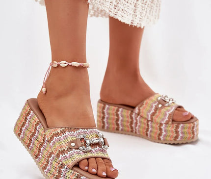 Sandales à plateforme tressées aux motifs colorés inspirés du Brésil, ornées de détails brillants sur la bride, parfaites pour un style tropical et festif, portées avec élégance par une personne habillée d'une jupe blanche en crochet et un bracelet de cheville en coquillages.
