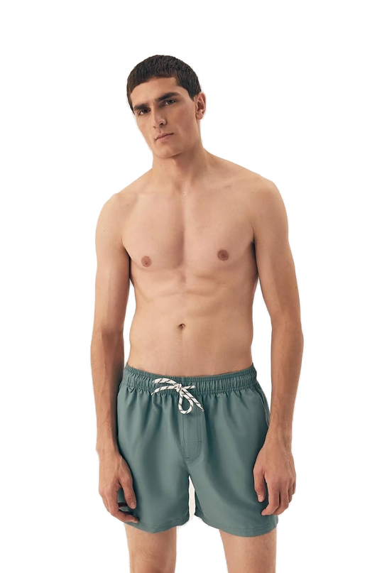 Homme portant un maillot de bain vert de style minimaliste inspiré de l'esprit détendu et vibrant des plages brésiliennes, conçu pour le confort et la liberté de mouvement. Modèle décontracté parfait pour des activités en plein air et des moments de détente au soleil.