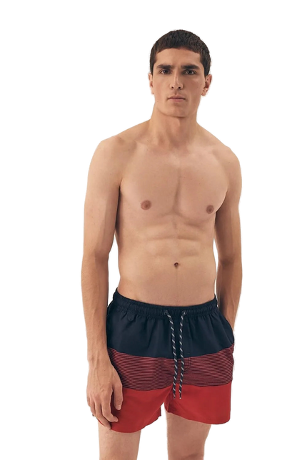 Homme portant un short de bain pour hommes rouge et noir à imprimé tendance, avec une taille élastique et des cordons ajustables. Modèle léger, à séchage rapide, avec une doublure intérieure pour plus de confort. Idéal pour la plage ou la piscine.