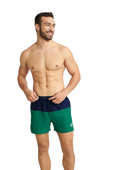 Homme souriant portant un maillot de bain GEM bicolore bleu marine et vert, conçu pour l'été et les activités nautiques, avec une coupe mi-cuisse, une taille élastique et un cordon de serrage. Le maillot arbore un emblème blanc sur le côté gauche avec le mot Summer.
