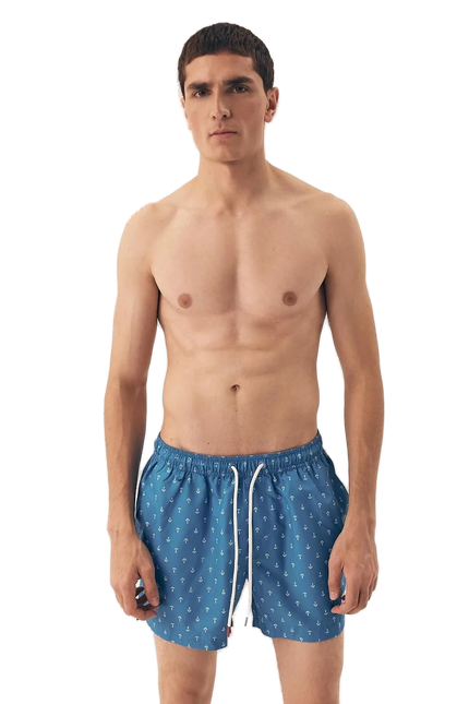 Homme portant un maillot de bain bleu à motifs d'ancres marines, inspiré des plages brésiliennes, alliant style décontracté et élégance tropicale. Parfait pour une journée au bord de l'eau ou une promenade en bord de plage, ce maillot reflète le lifestyle balnéaire moderne et intemporel.