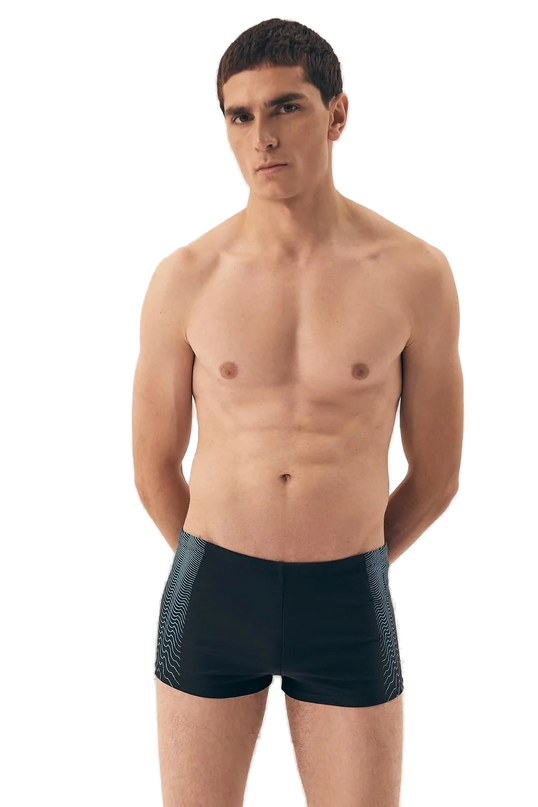 Homme portant un maillot de bain noir moderne et minimaliste, inspiré de l'élégance décontractée des plages brésiliennes comme Copacabana et Ipanema. Le design inclut des détails graphiques sur les côtés, incarnant l'esprit vibrant et énergique du Brésil. Idéal pour allier confort et style sur la plage.