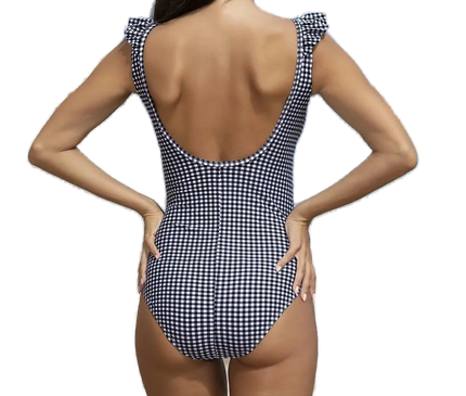 Maillot de bain une-pièce à carreaux noir et blanc avec dos échancré et volants aux épaules, porté sur une plage exotique avec vue sur la mer et des falaises en arrière-plan, incarnant l'élégance brésilienne et l'esprit tropical.