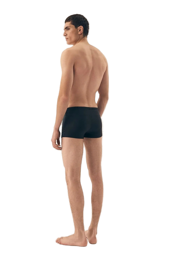 Homme portant un maillot de bain moderne et minimaliste noir, inspiré de l'élégance décontractée des plages brésiliennes telles que Copacabana et Ipanema, mettant en valeur le confort et le style.